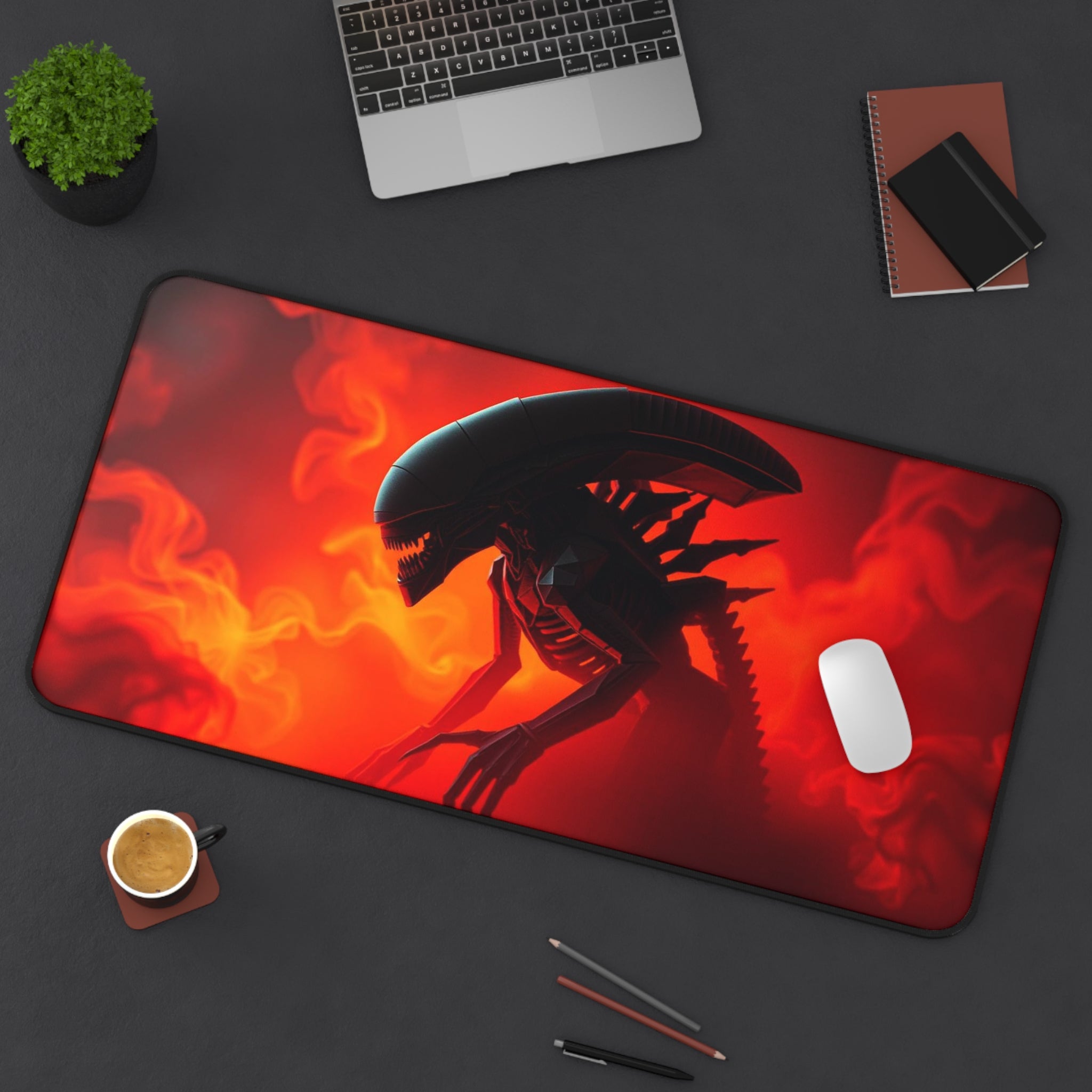 Desk setup with a large mouse pad featuring an alien design, laptop, mug, and office supplies.